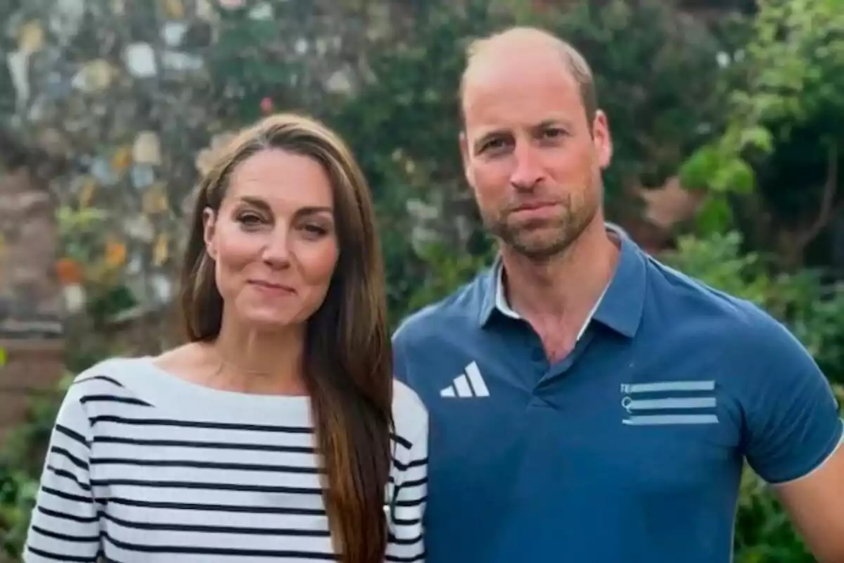 Kate Middleton amb una samarreta de ratlles i el príncep Guillem amb una samarreta blava posen junts a l'aire lliure amb un fons de vegetació i una paret de pedra.