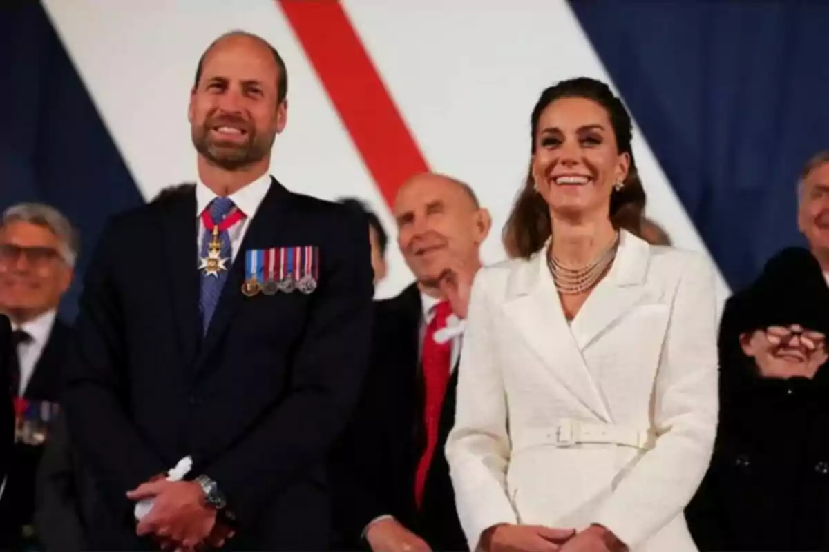 Un home i una dona somriuen mentre estan drets en un esdeveniment formal envoltats d'altres persones. Un home i una dona somriuen mentre estan drets en un esdeveniment formal envoltats d'altres persones.