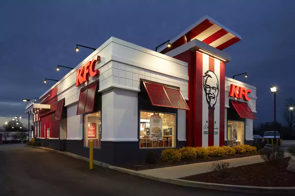 Un restaurant de menjar ràpid KFC il·luminat a la nit amb el logotip visible a la façana.