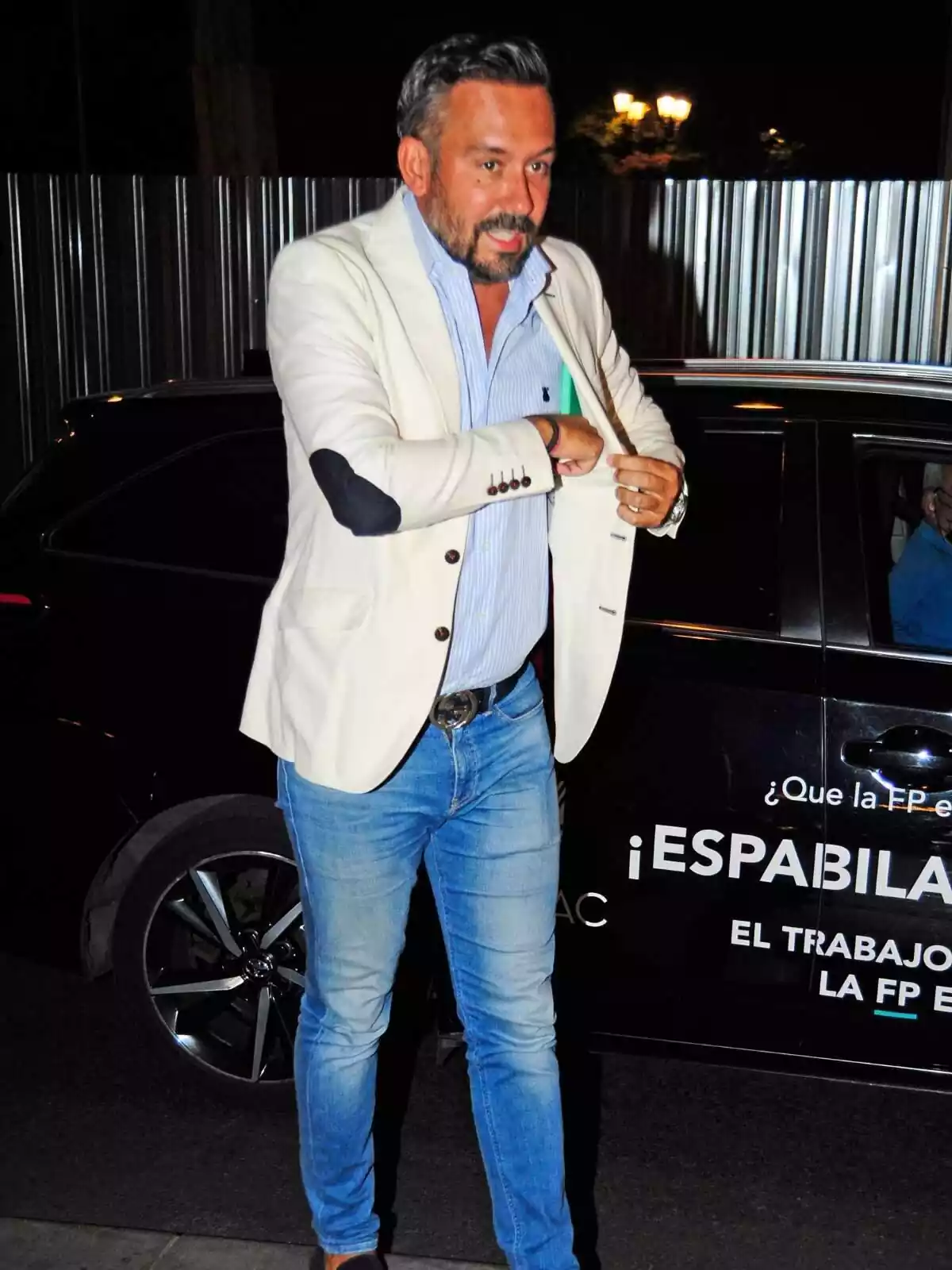 Foto vertical de Kike Calleja guardant un objecte a la seva americana blanca el 2023