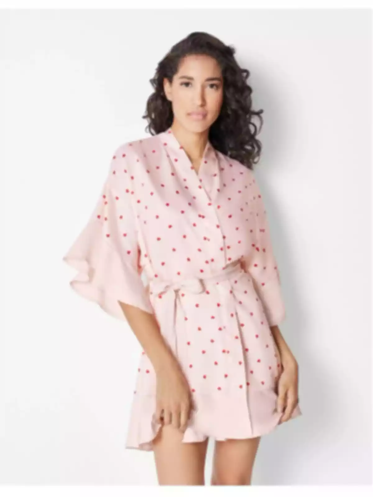 Dona amb cabell arrissat que porta un vestit curt rosa clar amb estampat de petits punts vermells i cinturó del mateix teixit Dona amb cabell arrissat que porta un vestit curt rosa clar amb estampat de petits punts vermells i cinturó del mateix teixit
