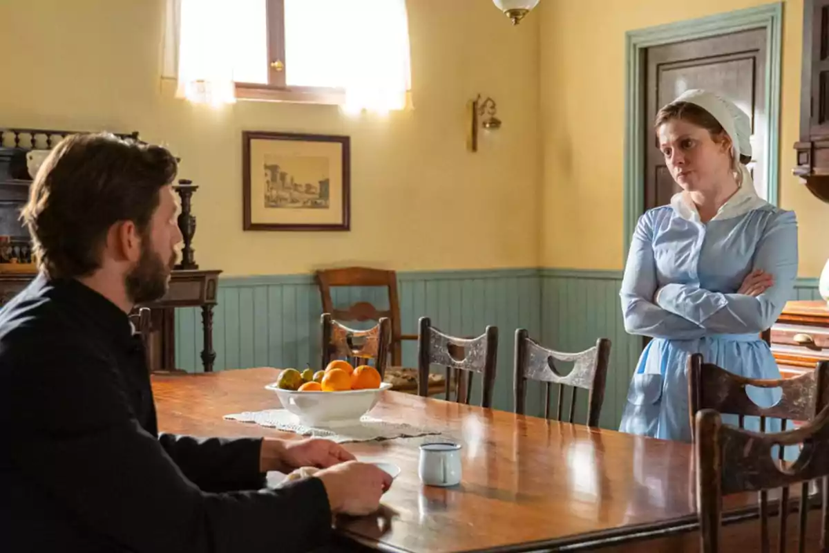 Samuel assegut a la taula d’un menjador antic conversa amb María vestida de minyona, que està dreta amb els braços creuats. Captura de ‘La Promesa’ Samuel assegut a la taula d’un menjador antic conversa amb María vestida de minyona, que està dreta amb els braços creuats. Captura de ‘La Promesa’