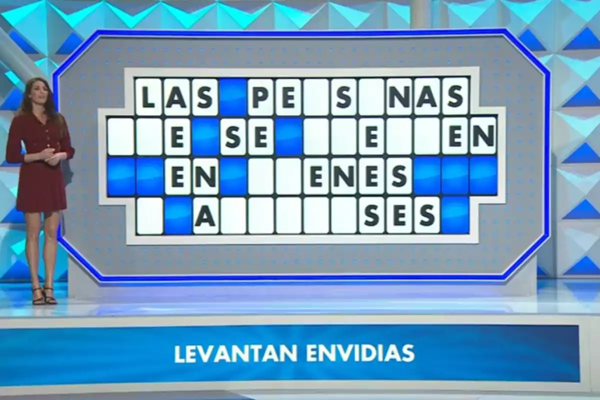 Laura Moure dempeus al costat d’un panell de lletres parcialment resoltes en un concurs de televisió amb la frase aixequen enveges a la part inferior. Captura de ‘La Ruleta de la Suerte’. Laura Moure dempeus al costat d’un panell de lletres parcialment resoltes en un concurs de televisió amb la frase aixequen enveges a la part inferior. Captura de ‘La Ruleta de la Suerte’.