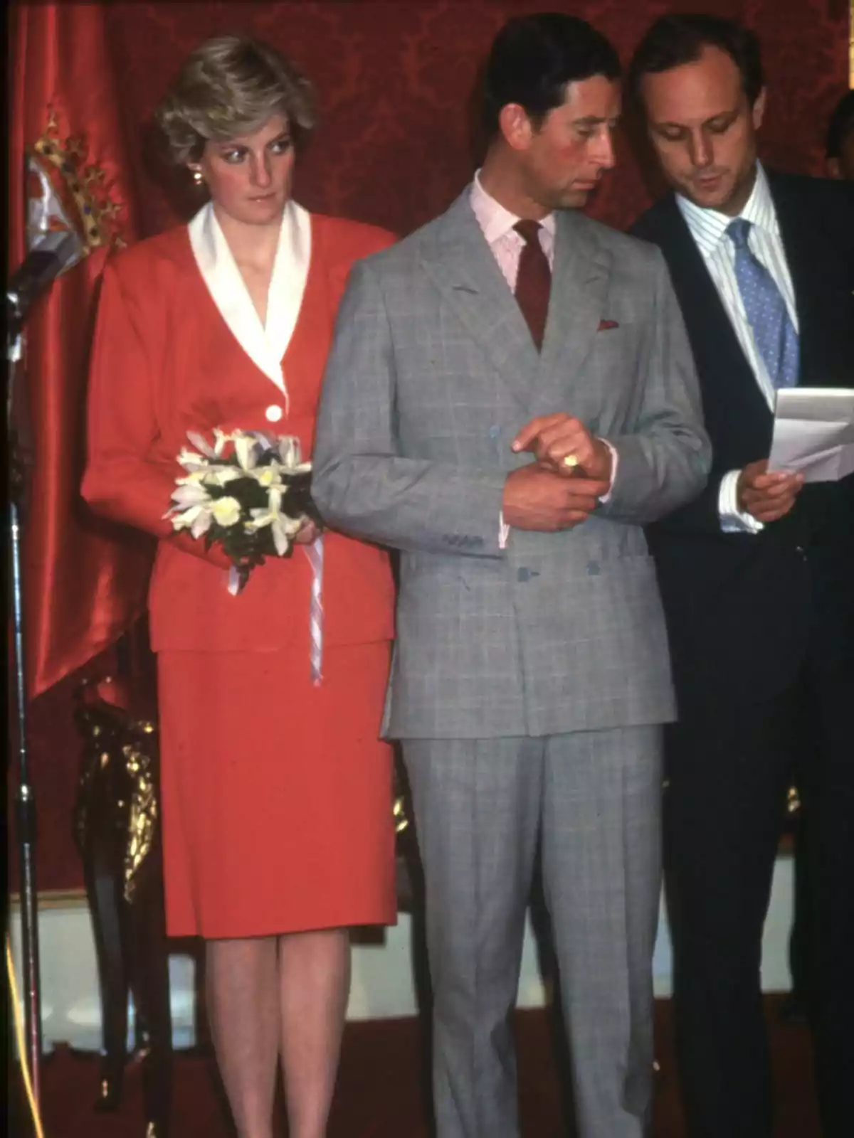 Lady Di amb un ram de flors i Carles III de vestit estan drets en un esdeveniment formal. Lady Di amb un ram de flors i Carles III de vestit estan drets en un esdeveniment formal.