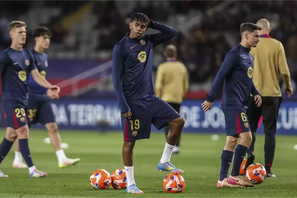 FC Barcelona players on the field during a training session, wearing dark blue training uniforms and surrounded by balls. FC Barcelona players on the field during a training session, wearing dark blue training uniforms and surrounded by balls.