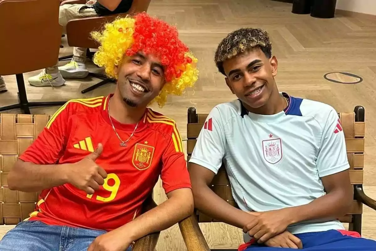 Lamine Yamal i el seu pare, asseguts en cadires, el pare amb una perruca de colors vermell i groc i una samarreta vermella de la selecció espanyola de futbol, i el fill amb una samarreta blanca de la mateixa selecció. Lamine Yamal i el seu pare, asseguts en cadires, el pare amb una perruca de colors vermell i groc i una samarreta vermella de la selecció espanyola de futbol, i el fill amb una samarreta blanca de la mateixa selecció.