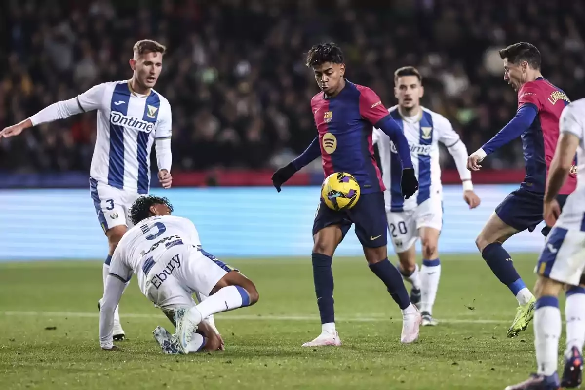 Jugadores de fútbol en acción durante un partido, uno de ellos controla el balón mientras otros observan.