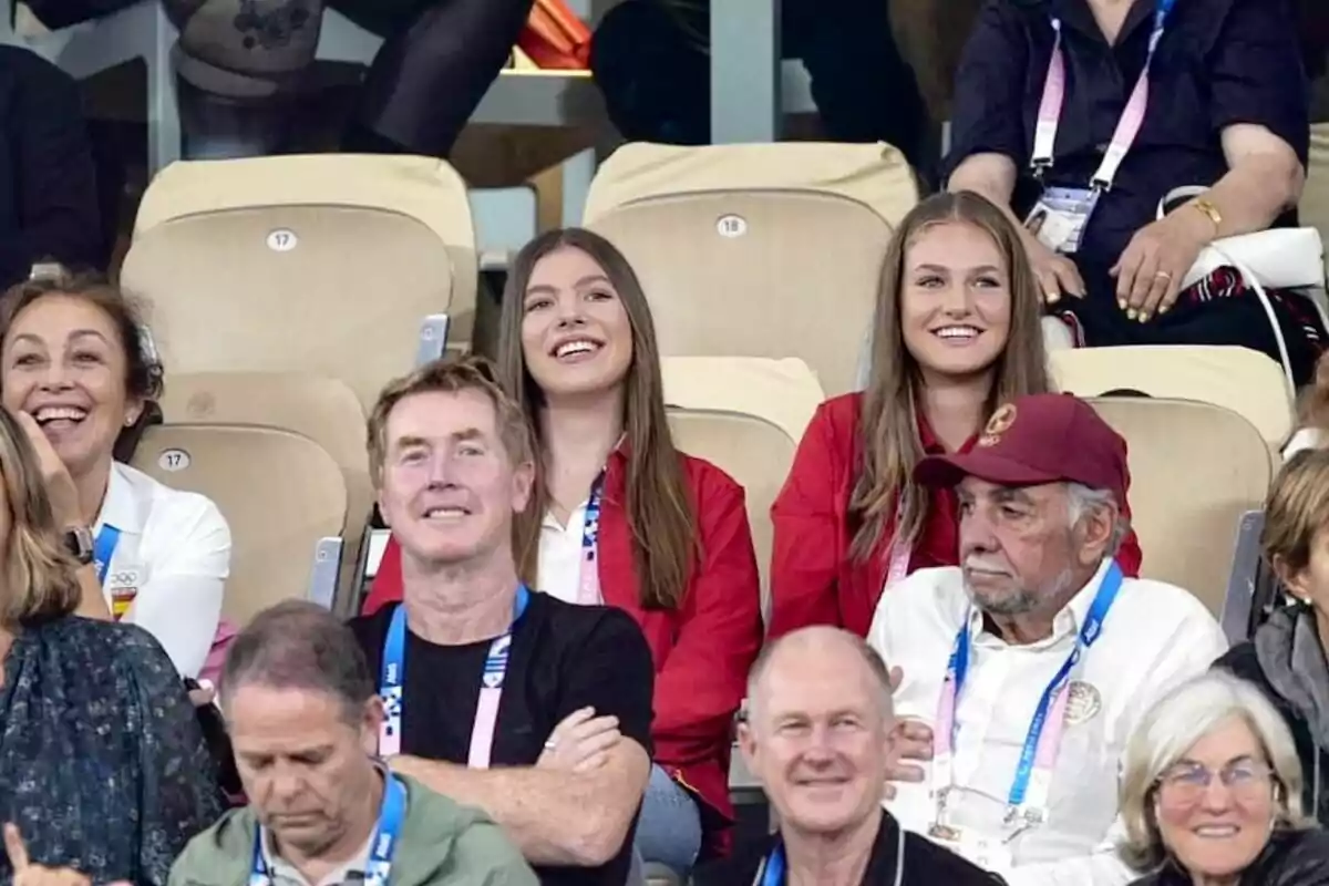 Un grupo de personas sonrientes y sentadas en las gradas de un evento deportivo. Un grupo de personas sonrientes y sentadas en las gradas de un evento deportivo.