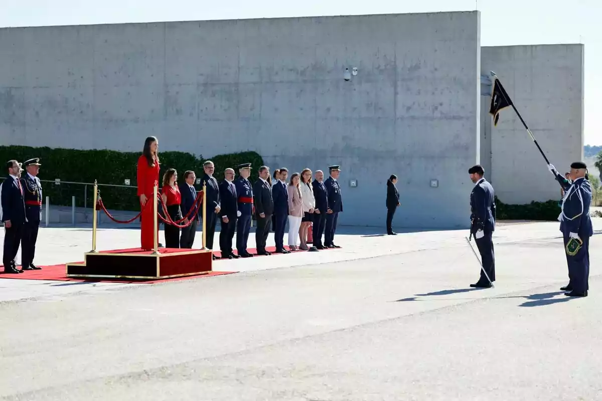 Cerimònia oficial amb Leonor dempeus en una plataforma vermella i diverses persones uniformades alineades al seu costat. Cerimònia oficial amb Leonor dempeus en una plataforma vermella i diverses persones uniformades alineades al seu costat.