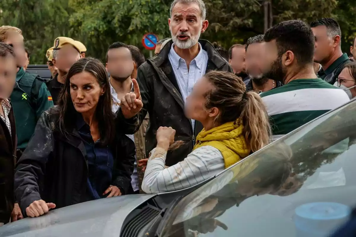 Letizia y Felipe VI conversando en un entorno al aire libre, con árboles y un coche en primer plano.