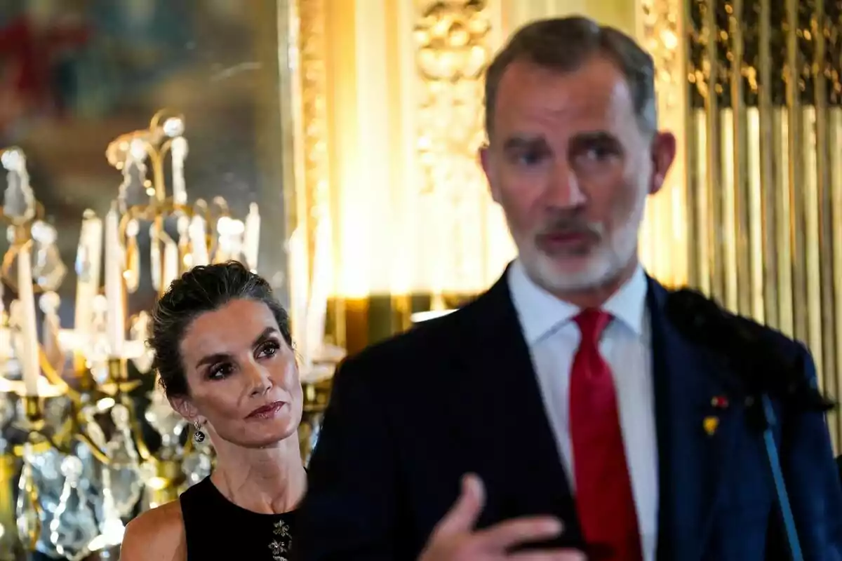 Letizia observa atentamente a Felipe VI que está hablando en un entorno elegante y bien iluminado. Letizia observa atentamente a Felipe VI que está hablando en un entorno elegante y bien iluminado.