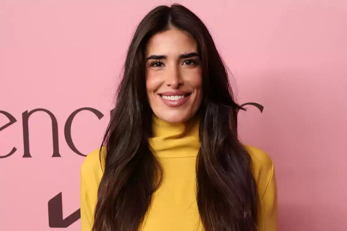 Lidia Torrent sonriendo, vistiendo un suéter amarillo, con un fondo rosa. Lidia Torrent sonriendo, vistiendo un suéter amarillo, con un fondo rosa.