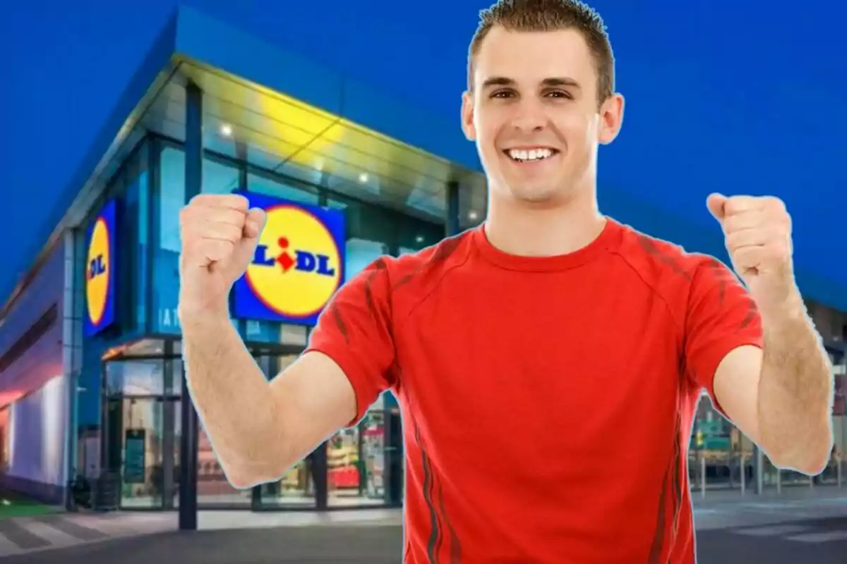 Un home somrient amb samarreta vermella aixeca els punys davant d'una botiga Lidl.