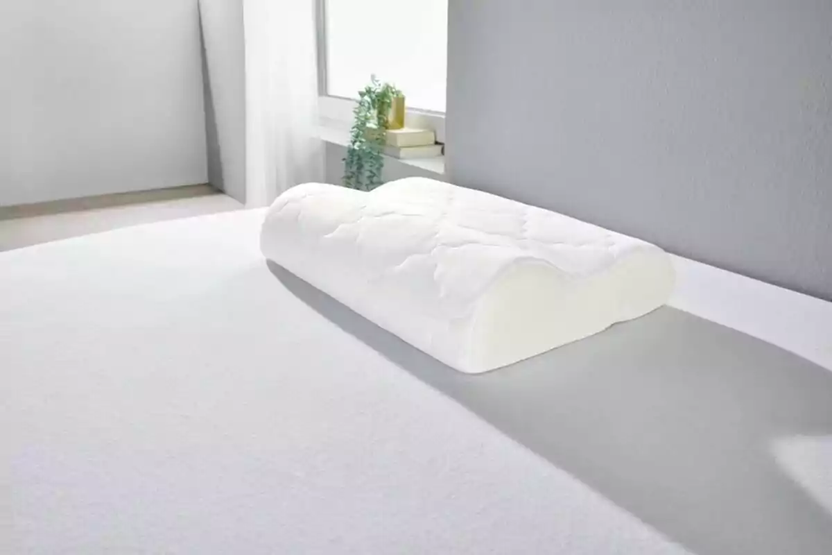 Un coixí ergonòmic blanc sobre un llit en una habitació il·luminada per la llum natural. Un coixí ergonòmic blanc sobre un llit en una habitació il·luminada per la llum natural.