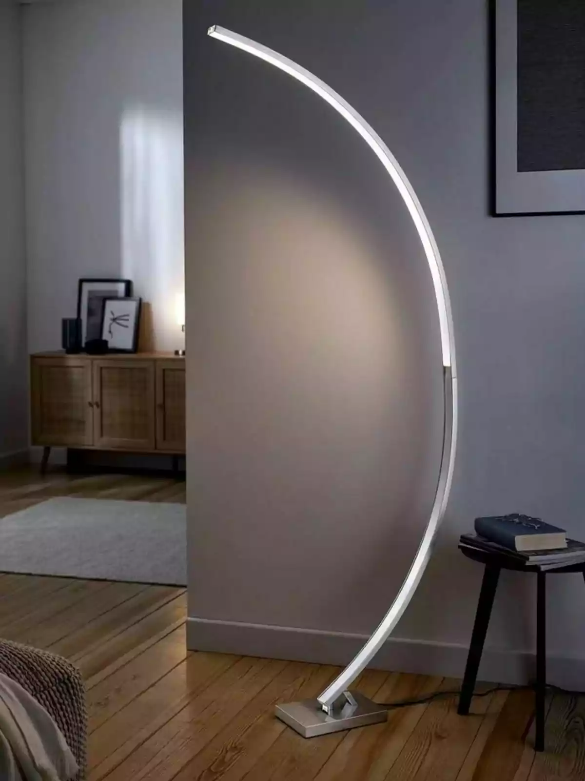 Làmpada de peu moderna amb disseny corbat encesa al costat d’una taula petita amb llibres en una habitació d’estil minimalista Làmpada de peu moderna amb disseny corbat encesa al costat d’una taula petita amb llibres en una habitació d’estil minimalista