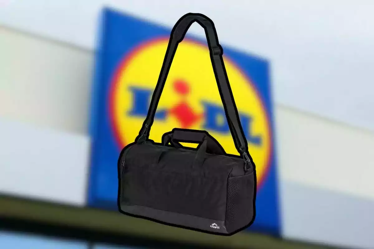 Una bossa d'esport negra amb corretja ajustable davant d'un fons desenfocat d'un logotip de supermercat.