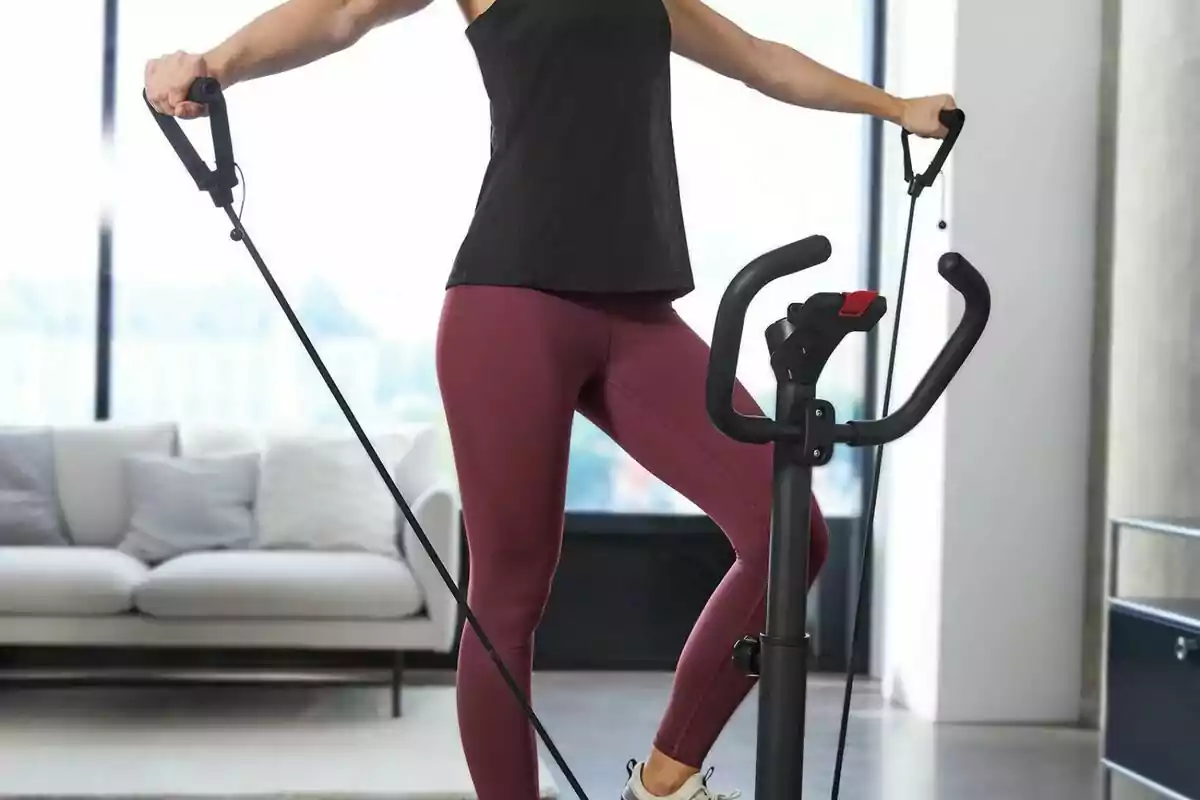 Persona fent exercici en una màquina el·líptica en una sala d'estar moderna. Persona fent exercici en una màquina el·líptica en una sala d'estar moderna.