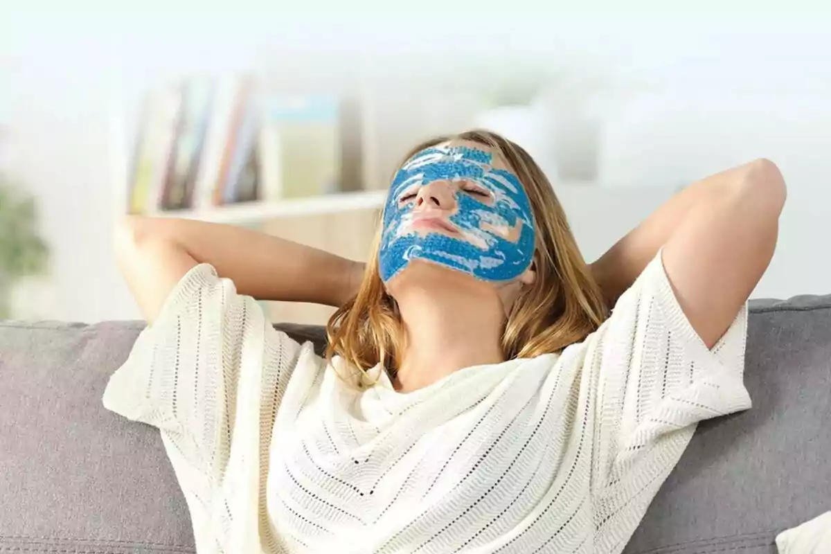 Dona relaxant-se en un sofà amb una màscara facial de gel blau Dona relaxant-se en un sofà amb una màscara facial de gel blau