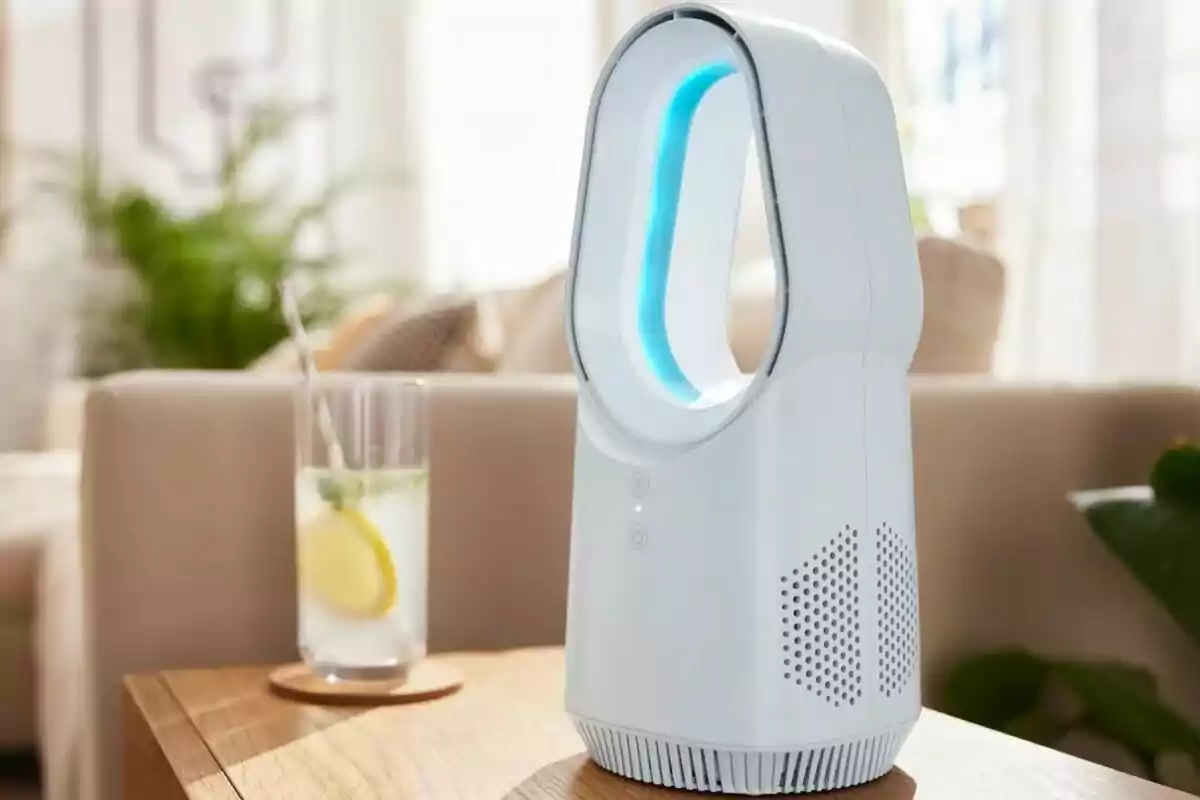 Un ventilador sense aspes de disseny modern sobre una taula de fusta al costat d’un got de llimonada amb una rodanxa de llimona i una palleta, en un ambient interior il·luminat i acollidor.