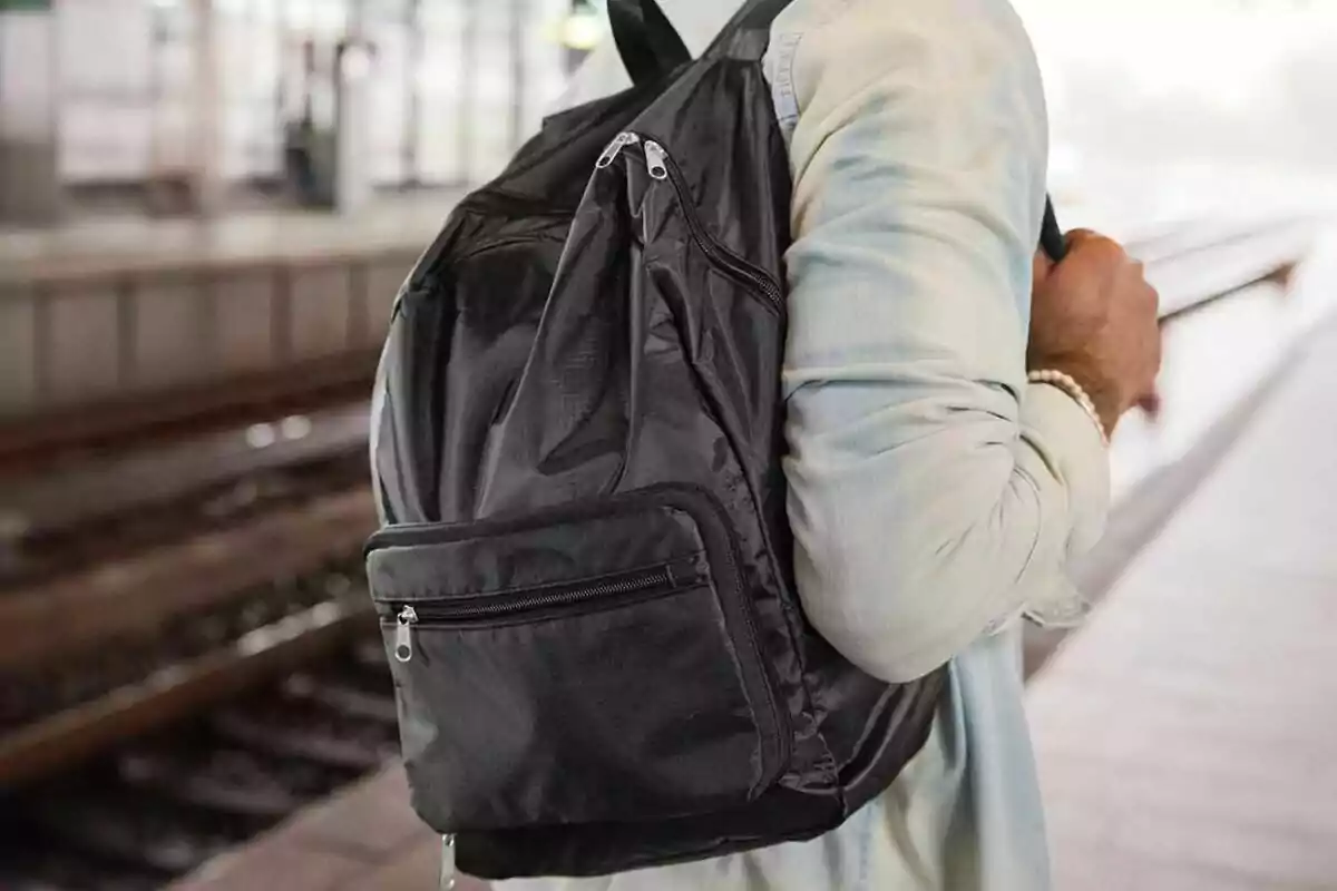 Persona amb camisa clara portant una motxilla negra en una estació de tren Persona amb camisa clara portant una motxilla negra en una estació de tren