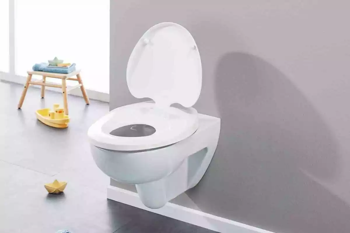 Inodor blanc muntat a la paret amb tapa oberta en un bany infantil, amb joguines i una cadira petita al fons. Inodor blanc muntat a la paret amb tapa oberta en un bany infantil, amb joguines i una cadira petita al fons.