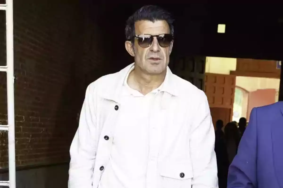 Luis Figo amb ulleres de sol i jaqueta blanca camina per un passadís fosc. Luis Figo amb ulleres de sol i jaqueta blanca camina per un passadís fosc.