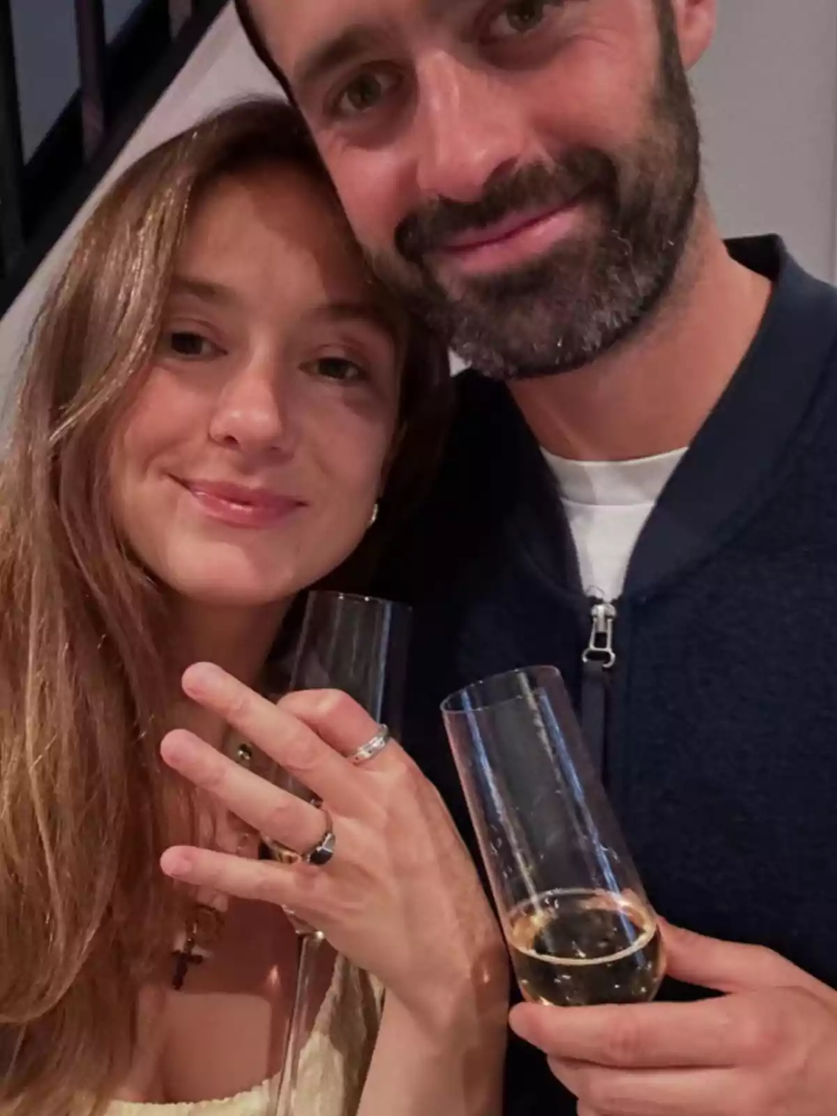 Parella somrient brindant amb copes de xampany mentre la dona mostra un anell a la seva mà Parella somrient brindant amb copes de xampany mentre la dona mostra un anell a la seva mà