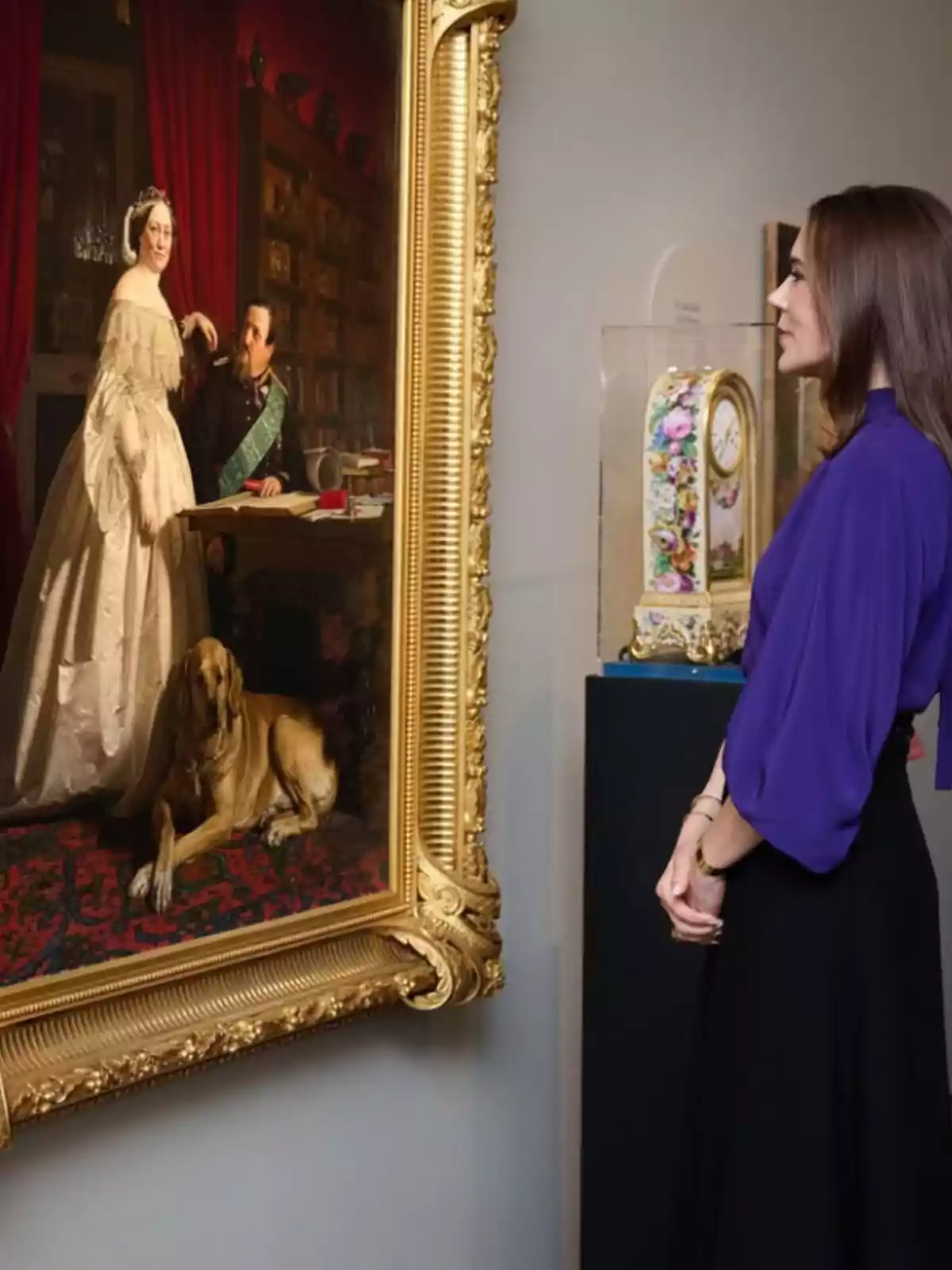Una dona observa atentament un gran quadre emmarcat que representa una parella elegant i un gos en una habitació decorada. Una dona observa atentament un gran quadre emmarcat que representa una parella elegant i un gos en una habitació decorada.