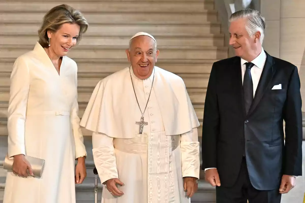 Matilde and Philippe of Belgium, along with Pope Francis, dressed formally, pose together in an elegant setting with stairs in the background. Matilde and Philippe of Belgium, along with Pope Francis, dressed formally, pose together in an elegant setting with stairs in the background.