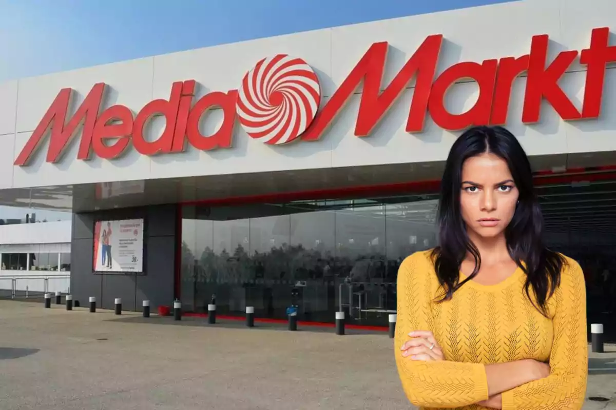 Una dona amb suèter groc està dreta davant d'una botiga MediaMarkt amb expressió seriosa.