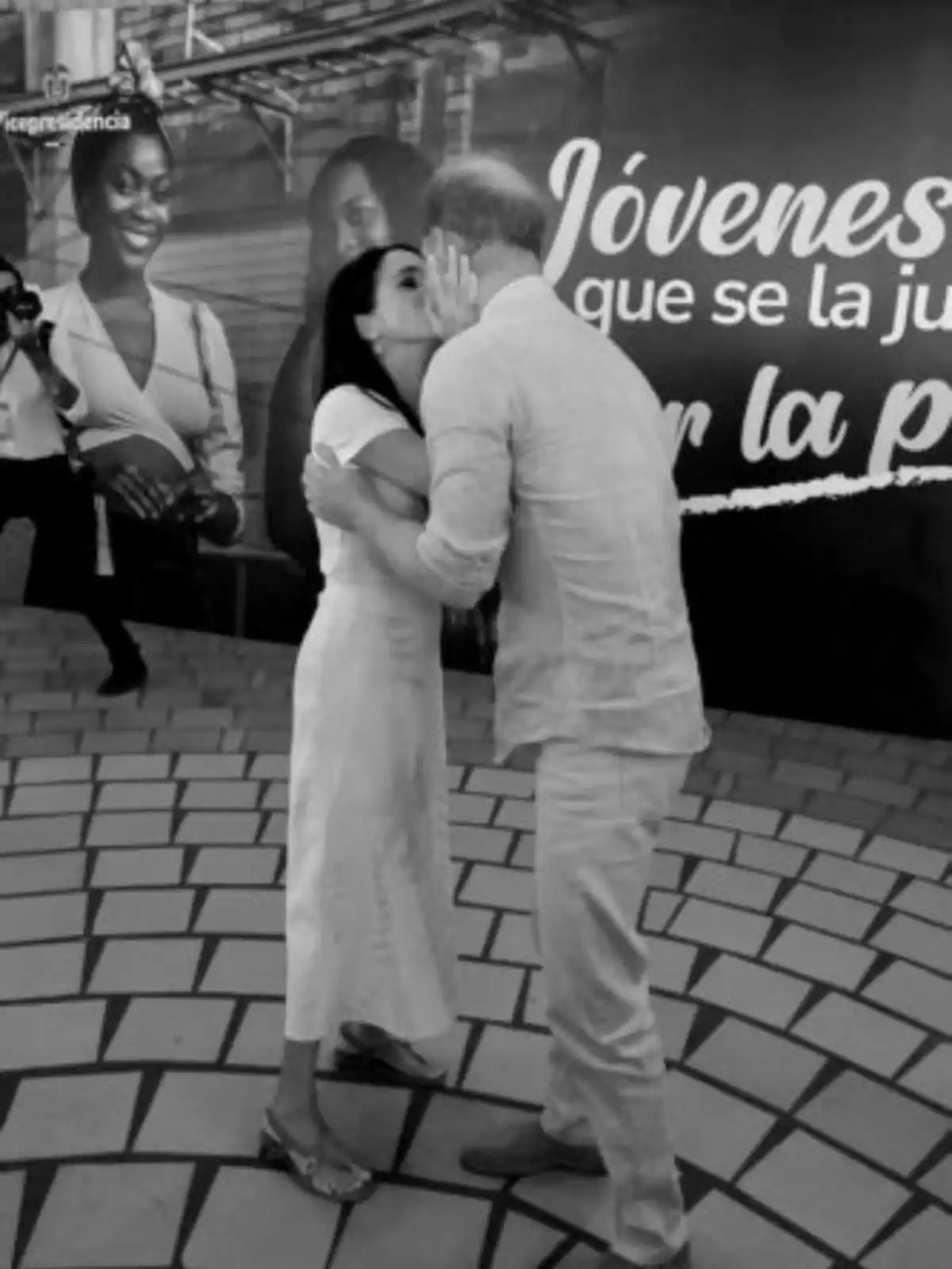 Meghan Markle i el príncep Harry s'abraça i es fa un petó a la galta davant d'un cartell que diu Meghan Markle i el príncep Harry s'abraça i es fa un petó a la galta davant d'un cartell que diu