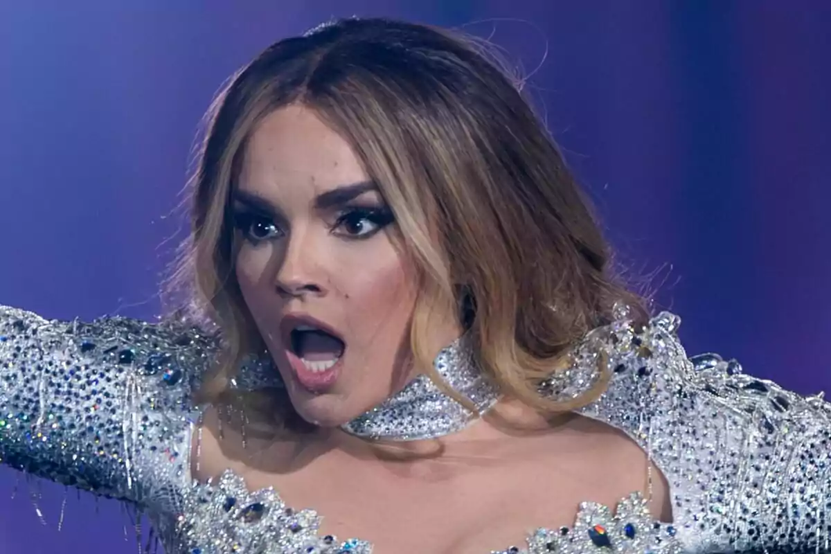 Melody amb expressió de sorpresa a l'escenari d'Eurovisió, vestida amb un vestit brillant i decorat amb pedreria. Melody amb expressió de sorpresa a l'escenari d'Eurovisió, vestida amb un vestit brillant i decorat amb pedreria.