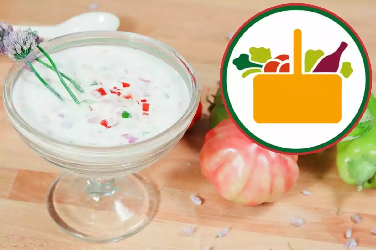 Un bol de vidre amb una sopa blanca i trossos de vegetals, decorat amb flors, amb un logotip d'una cistella de vegetals. Un bol de vidre amb una sopa blanca i trossos de vegetals, decorat amb flors, amb un logotip d'una cistella de vegetals.