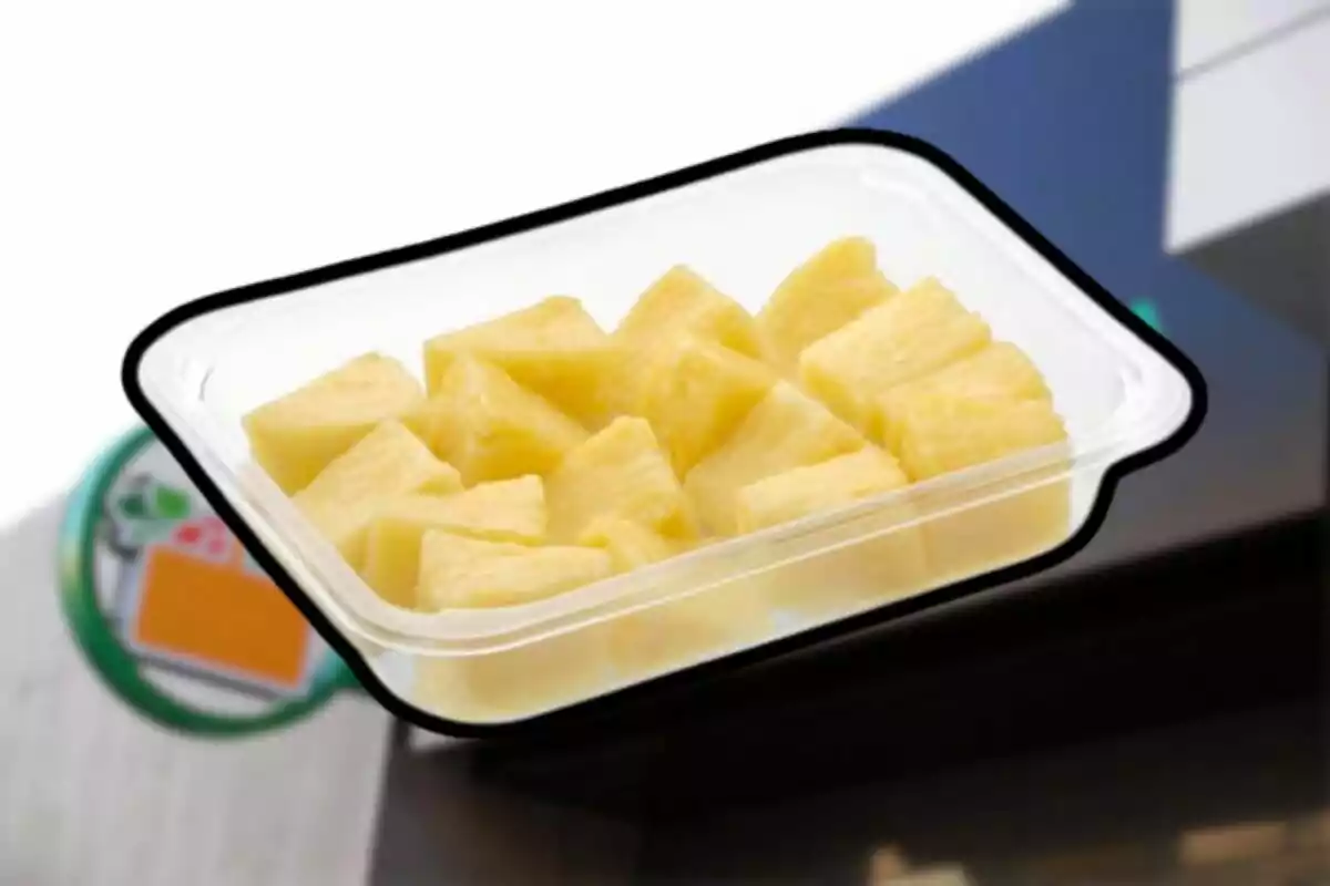 Envàs de plàstic transparent amb trossos de pinya groga sobre un fons difuminat Envàs de plàstic transparent amb trossos de pinya groga sobre un fons difuminat