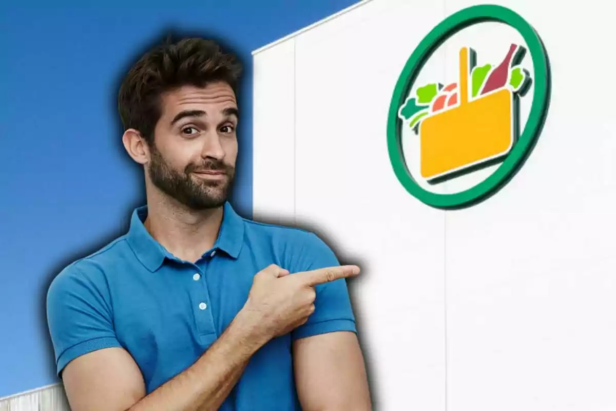 Home amb camisa blava assenyalant un logotip de supermercat en una paret blanca.