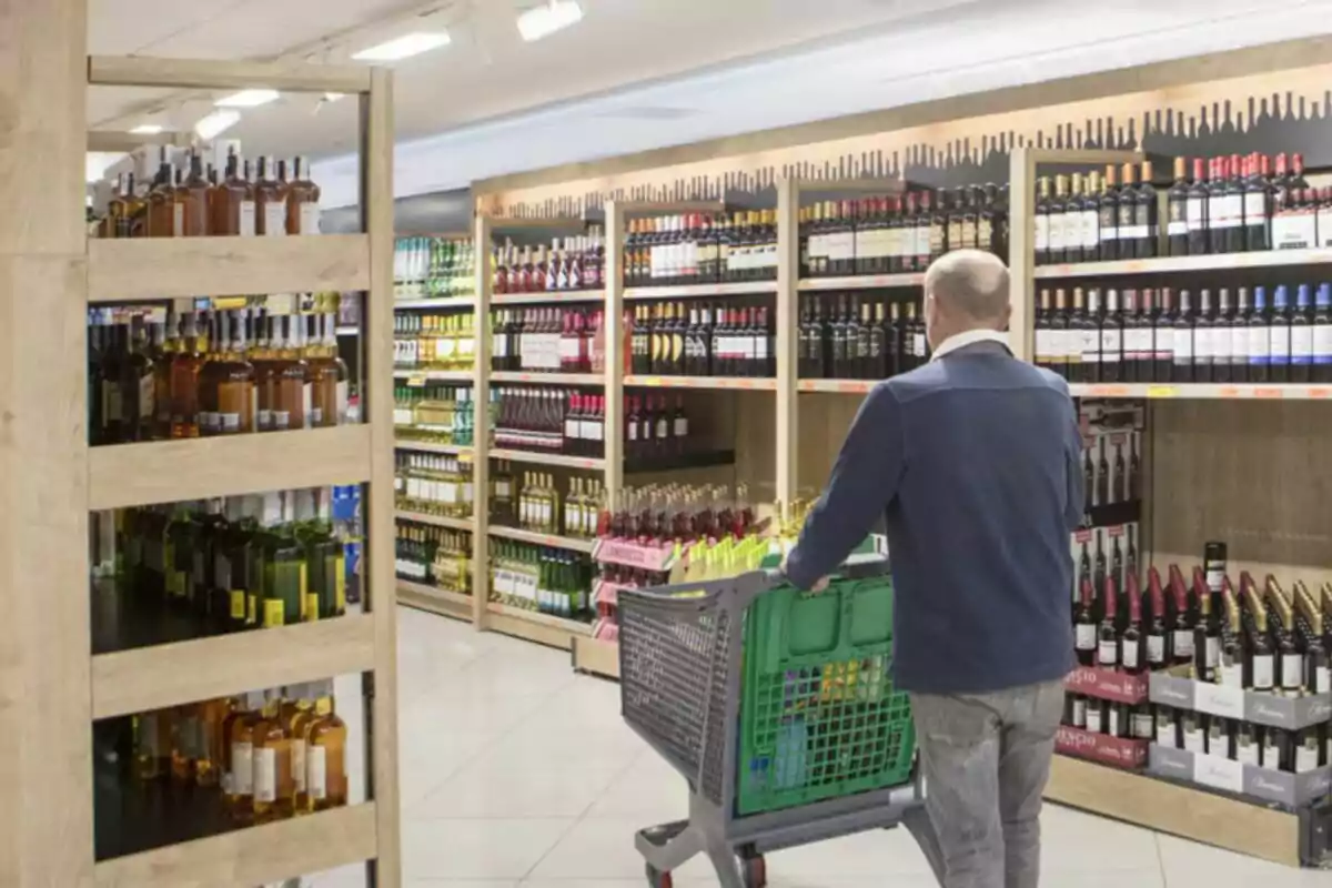 Home empenyent un carro de la compra a la secció de vins i licors d’un supermercat Home empenyent un carro de la compra a la secció de vins i licors d’un supermercat