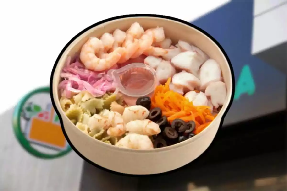 Amanida de marisc amb gambes, pop, pasta de colors, pastanaga ratllada, olives negres, ceba morada i amaniment en un recipient rodó Amanida de marisc amb gambes, pop, pasta de colors, pastanaga ratllada, olives negres, ceba morada i amaniment en un recipient rodó