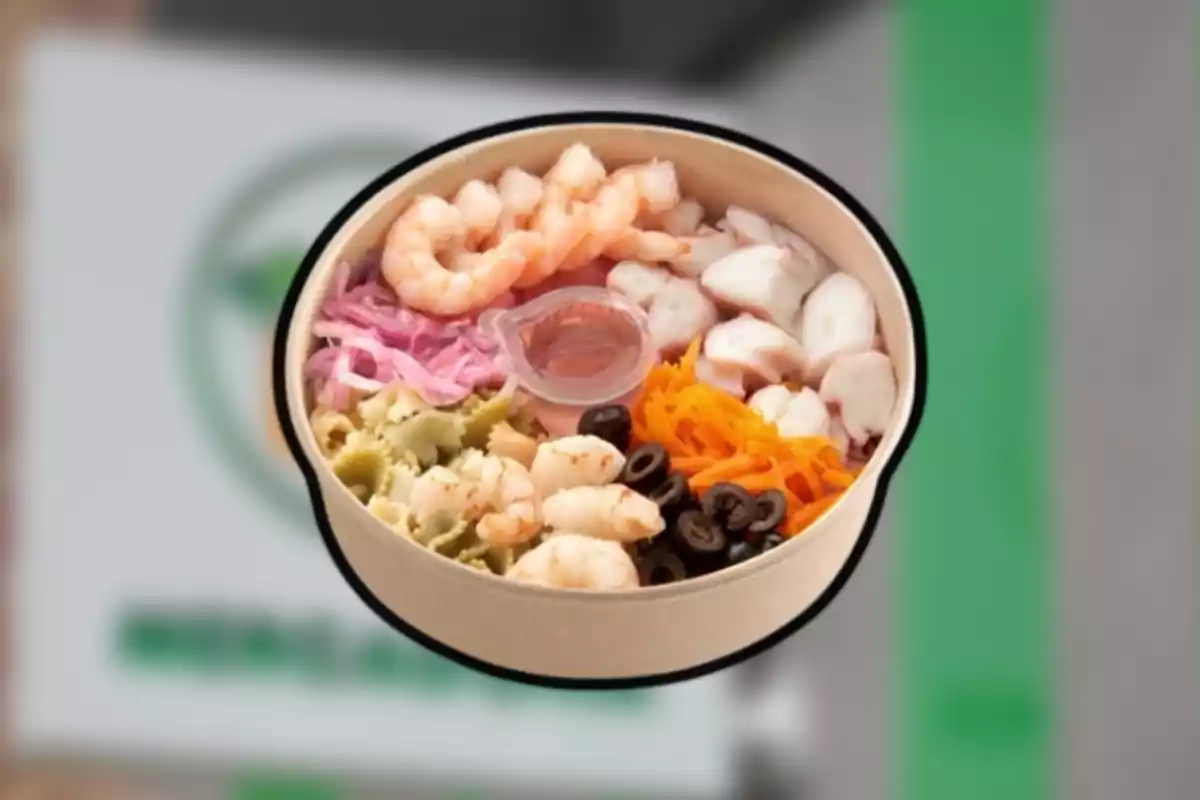 Un bowl de cartró amb gambetes, pop, pasta, pastanaga ratllada, ceba morada, olives negres i un amaniment al center. Un bowl de cartró amb gambetes, pop, pasta, pastanaga ratllada, ceba morada, olives negres i un amaniment al center.