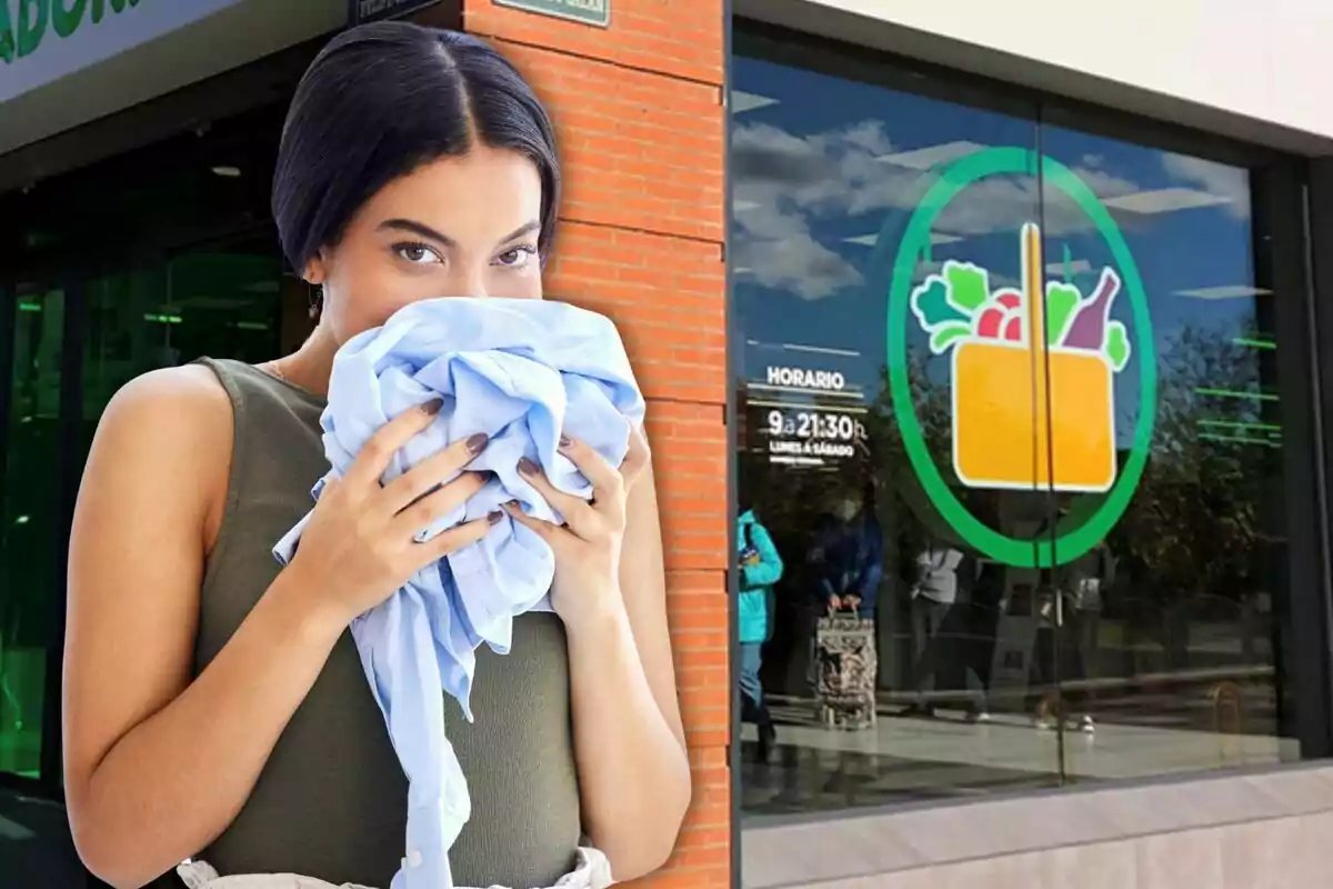 Dona sostenint i olorant una peça de roba blava davant de l’entrada d’un supermercat amb un logotip de cistella de la compra a la finestra