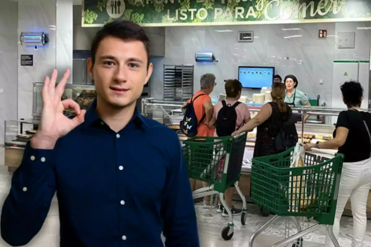 Un home amb camisa blava fa un gest d'aprovació amb la mà mentre al fons diverses persones amb carretons de supermercat esperen en un taulell de menjar.