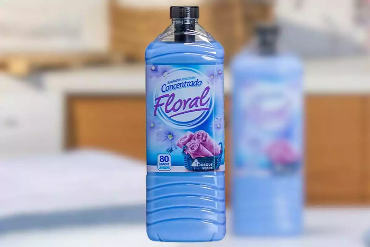 Ampolla de suavitzant blau amb etiqueta floral i tovalloles roses al centre de la imatge Ampolla de suavitzant blau amb etiqueta floral i tovalloles roses al centre de la imatge