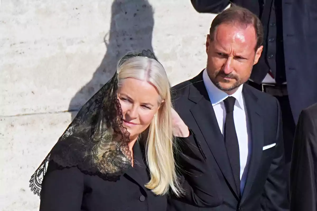 Mette-Marit in a black veil and Prince Haakon in a dark suit are together at a formal event. Mette-Marit in a black veil and Prince Haakon in a dark suit are together at a formal event.