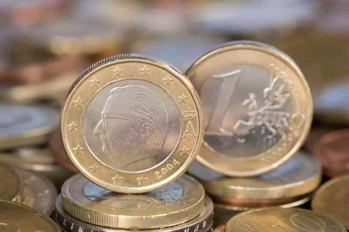 Dos monedes d'euro en postura vertical damunt de moltes altres monedes d'euro en postura plana