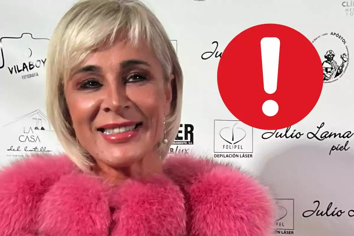 Ana María Aldón amb cabell ros i abric rosa posant davant d'un fons amb logotips i una icona d'advertència en vermell.