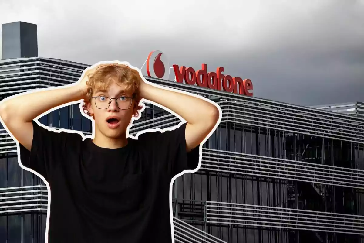 Un jove amb expressió de sorpresa es troba davant d'un edifici modern amb el logotip de Vodafone a la part superior.