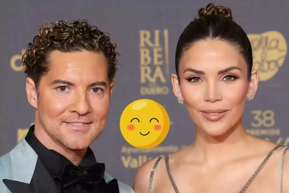 David Bisbal i Rosanna Zanetti posen juntes en un esdeveniment formal amb un fons que mostra logotips i text, i un emoji somrient està superposat al centre de la imatge.