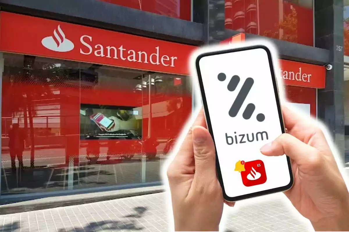 Una persona sosté un telèfon mòbil amb el logotip de Bizum davant d'una sucursal del banc Santander.