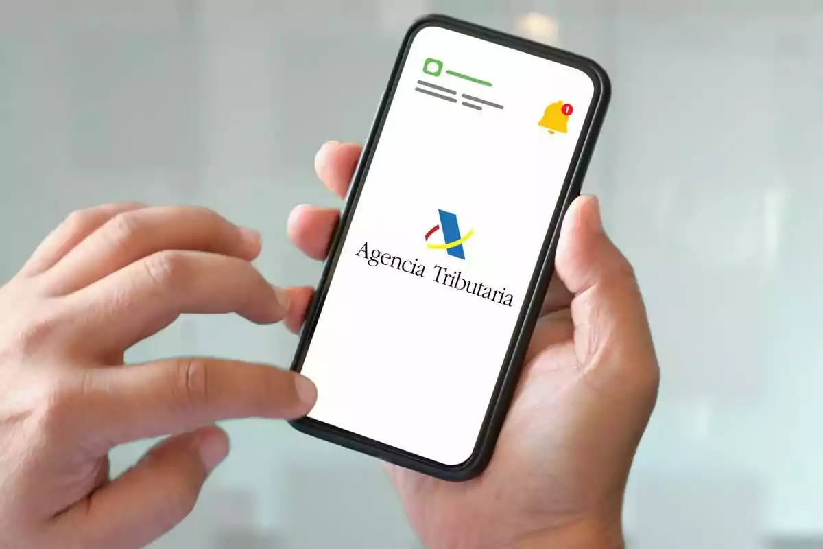 Persona sostenint un telèfon mòbil que mostra el logotip de l'Agència Tributària a la pantalla.