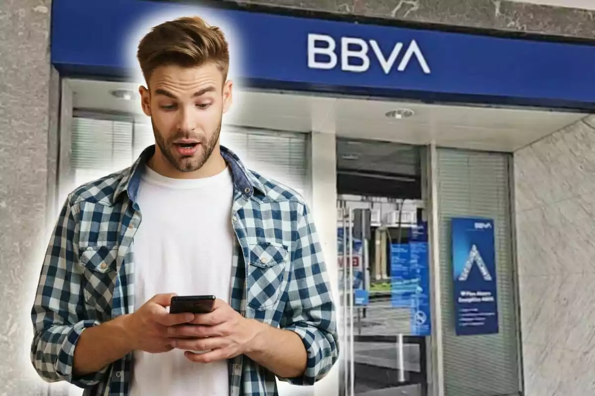 Un home sorprès mirant el telèfon davant una sucursal de BBVA.