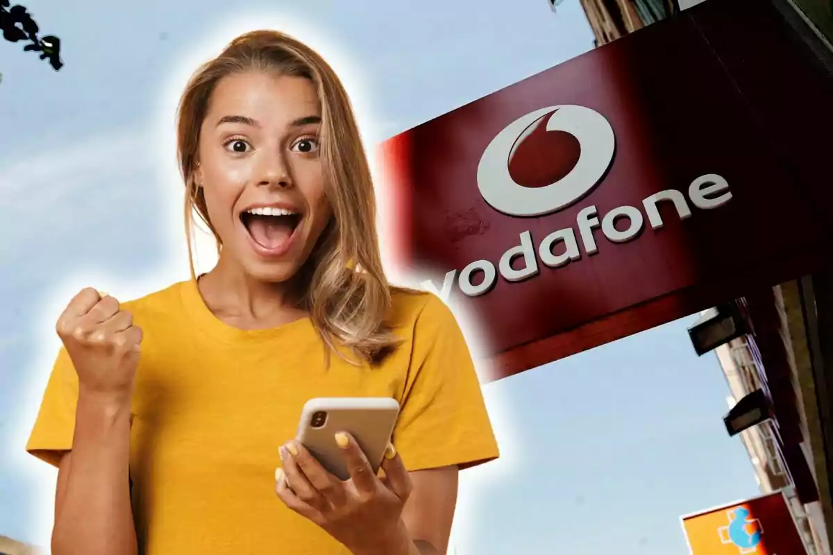 Dona emocionada amb samarreta groga sostenint un telèfon mòbil davant d'un cartell de Vodafone.